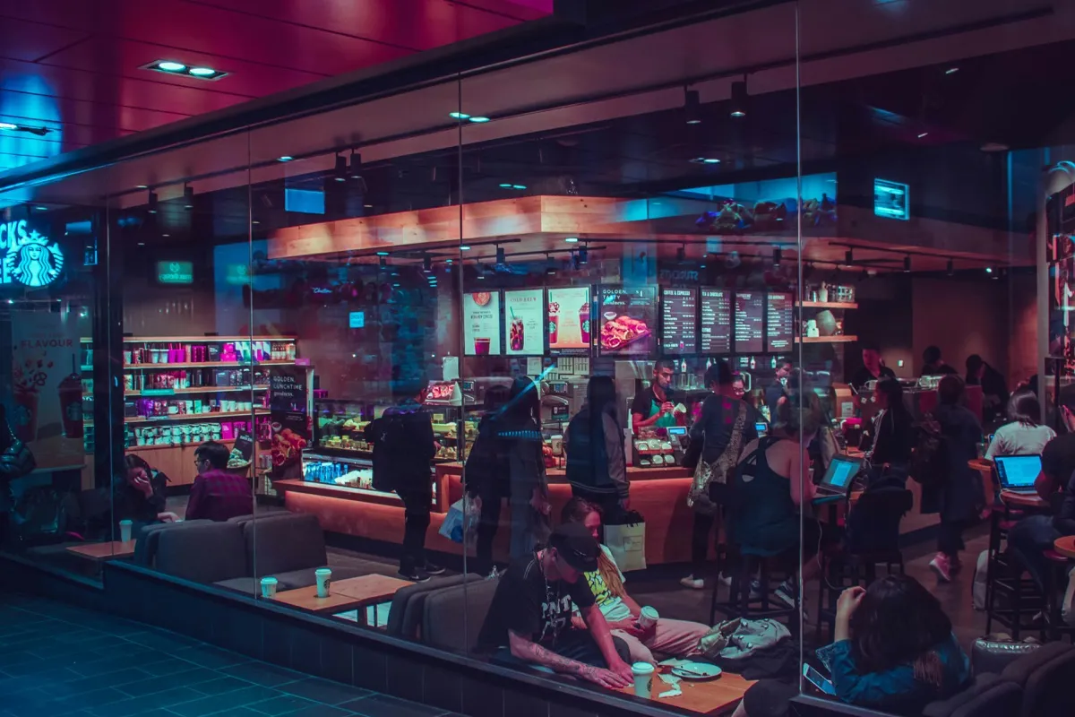 A busy café at night with people working on laptops and queuing at the counter.