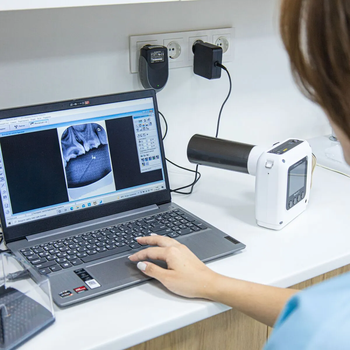 A clinician in scrubs reviewing a scan on a laptop with a handheld diagnostic device.