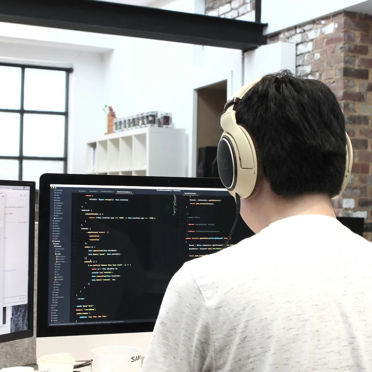 A developer wearing headphones works on code at a large monitor in a brick-walled studio.