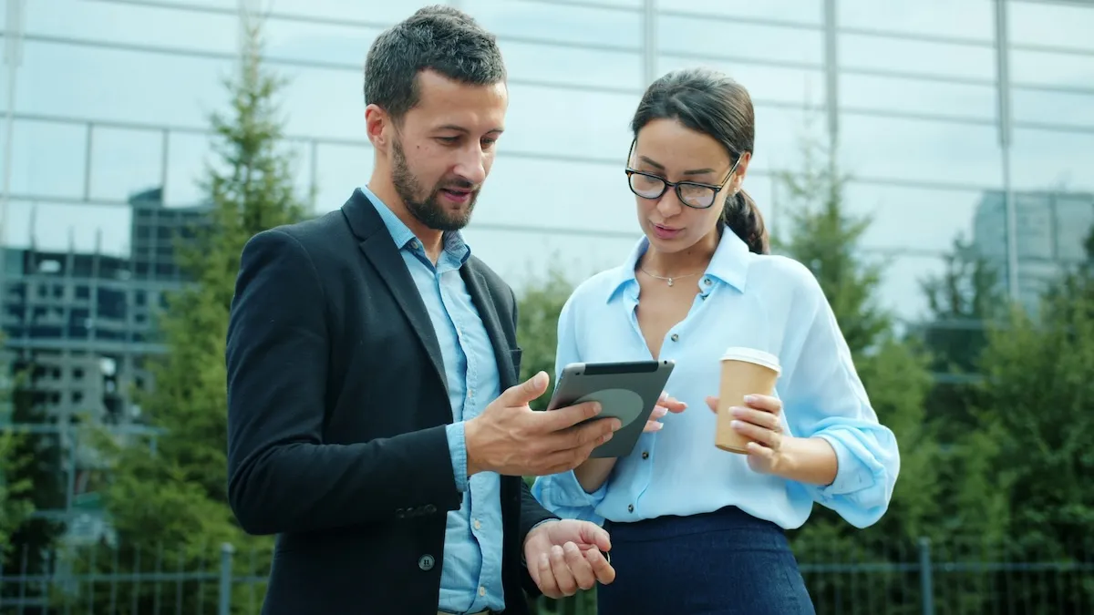 Two colleagues reviewing something on a tablet outside a glass office building.