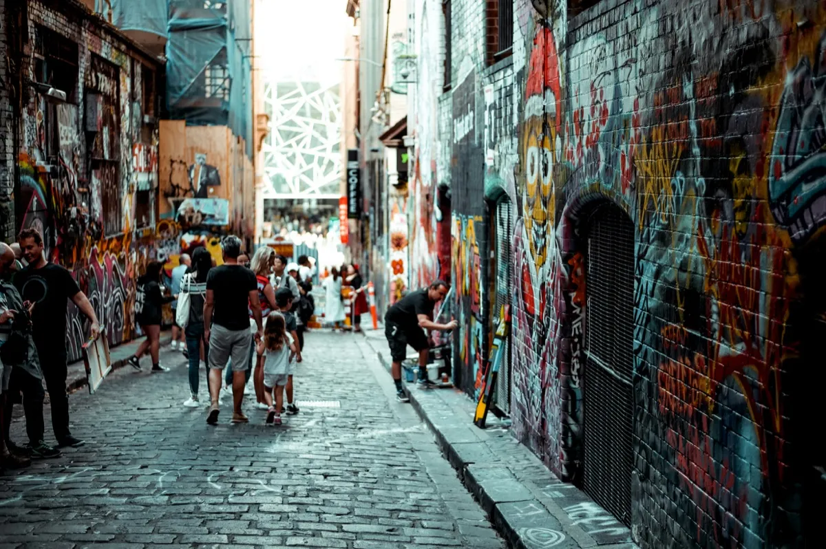 People walking through Melbourne's Hosier Lane, its walls covered in colourful street-art graffiti.