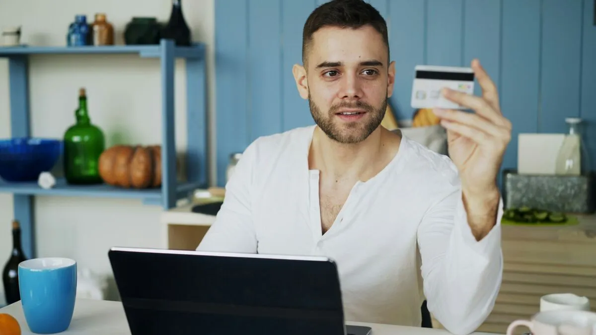A man holding a credit card while shopping online at a laptop.