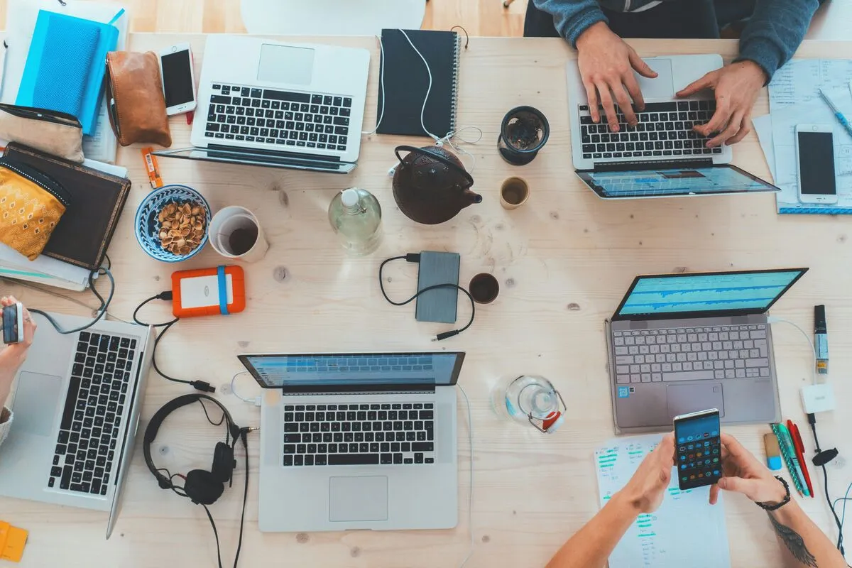 An overhead view of a shared desk covered in laptops, devices, and a phone as a team works.
