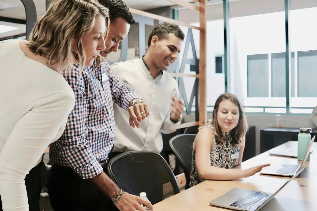A team gathered around a laptop reviewing work together in an office.