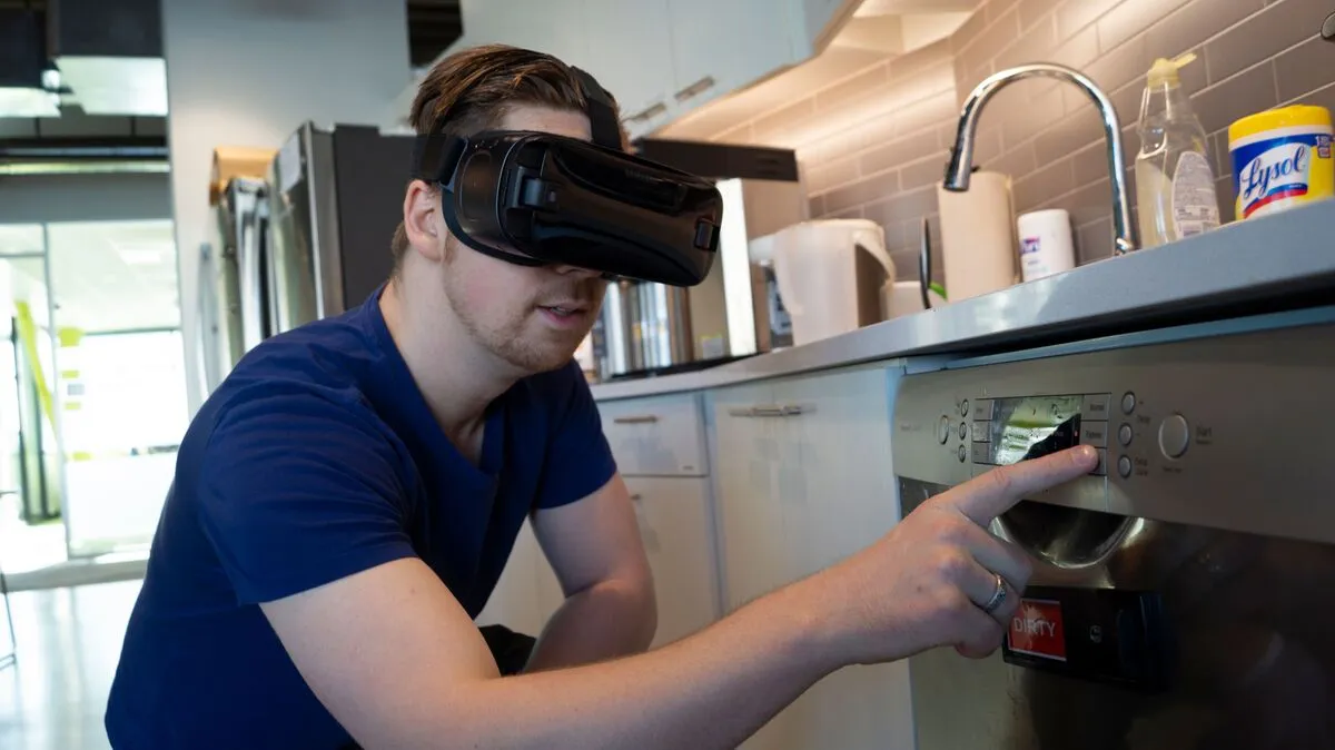 A man wearing a VR headset squints as he reaches to press a button on his dishwasher, a red 'DIRTY' magnet on the door.